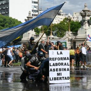 Los manifestantes se protegen detrás de una pancarta con el lema «La reforma laboral mata mi libertad» de un cañón de agua disparado por la policía antidisturbios durante una protesta convocada por sindicalistas contra el debate sobre la reforma laboral que se celebra en el Congreso Nacional de Buenos Aires el 11 de febrero de 2026.