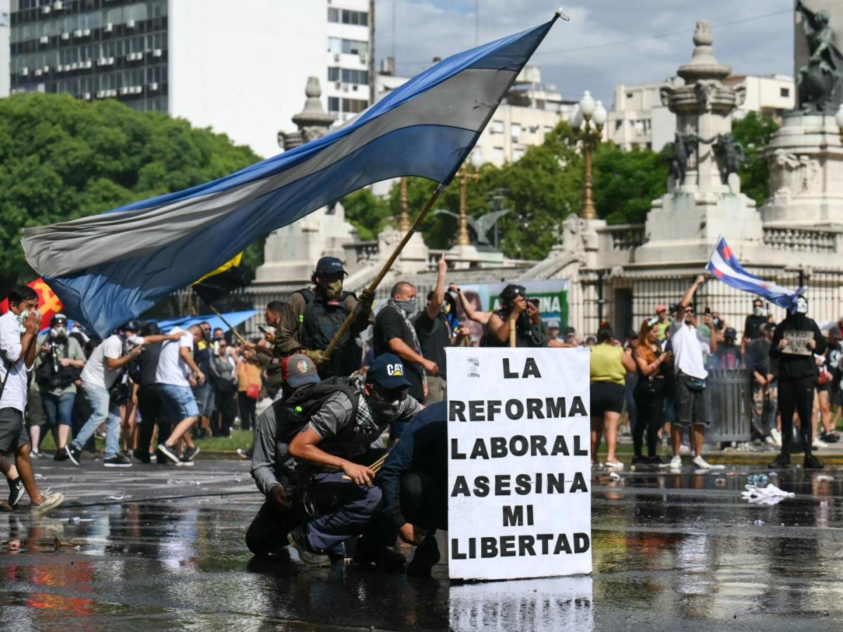 Los manifestantes se protegen detrás de una pancarta con el lema «La reforma laboral mata mi libertad» de un cañón de agua disparado por la policía antidisturbios durante una protesta convocada por sindicalistas contra el debate sobre la reforma laboral que se celebra en el Congreso Nacional de Buenos Aires el 11 de febrero de 2026.