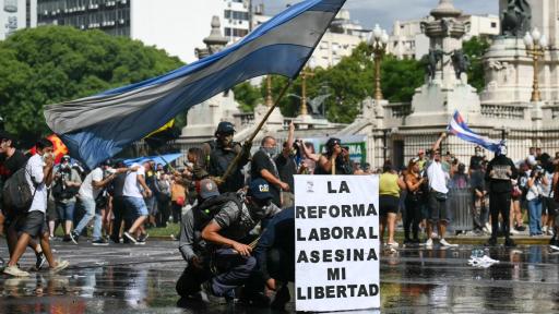 Los manifestantes se protegen detrás de una pancarta con el lema «La reforma laboral mata mi libertad» de un cañón de agua disparado por la policía antidisturbios durante una protesta convocada por sindicalistas contra el debate sobre la reforma laboral que se celebra en el Congreso Nacional de Buenos Aires el 11 de febrero de 2026.