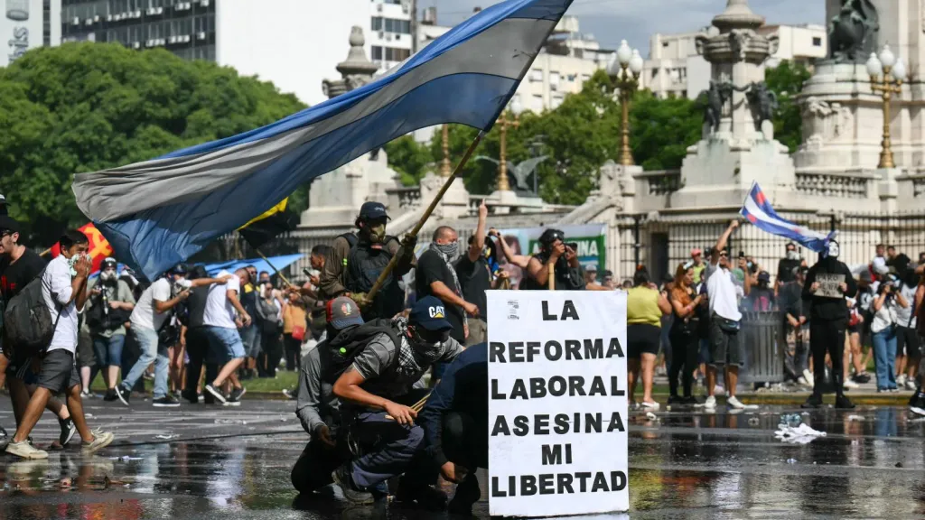 Los manifestantes se protegen detrás de una pancarta con el lema «La reforma laboral mata mi libertad» de un cañón de agua disparado por la policía antidisturbios durante una protesta convocada por sindicalistas contra el debate sobre la reforma laboral que se celebra en el Congreso Nacional de Buenos Aires el 11 de febrero de 2026.