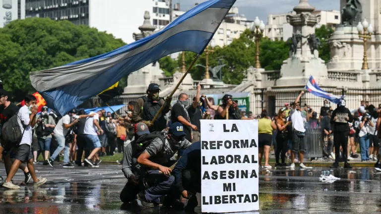Los manifestantes se protegen detrás de una pancarta con el lema «La reforma laboral mata mi libertad» de un cañón de agua disparado por la policía antidisturbios durante una protesta convocada por sindicalistas contra el debate sobre la reforma laboral que se celebra en el Congreso Nacional de Buenos Aires el 11 de febrero de 2026.